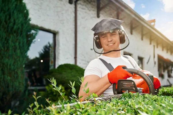 Caucásico hombre poda seto con trimmer eléctrico — Foto de Stock