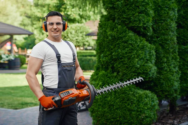 Mann i uniform med elektrisk hekksaks utendørs – stockfoto