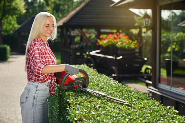Female gardener cutting bushes with electric trimmer — Stock Photo, Image