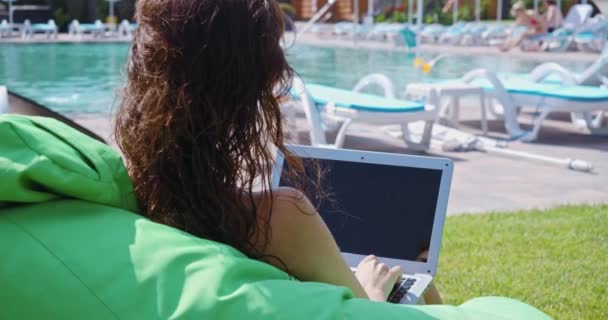Kvinne som arbeider på laptop nær svømmebassenget – stockvideo