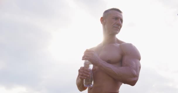 Hombre fuerte sin camisa bebiendo agua después de un entrenamiento intenso — Vídeo de stock