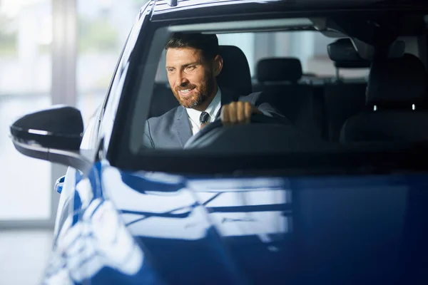 Hombre positivo en ropa formal examinando el coche en el salón moderno —  Fotos de Stock