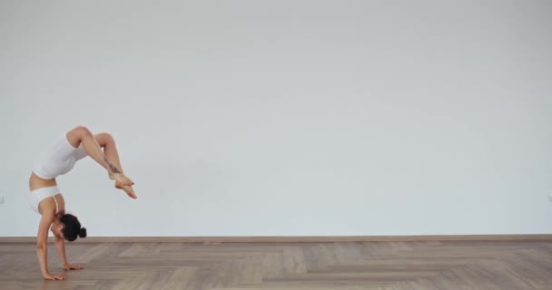 Mulher flexível em sportswear fazendo roda posar dentro de casa — Vídeo de Stock
