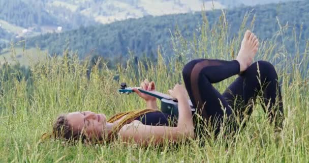 Γυναίκα ξαπλωμένη στο γρασίδι και παίζοντας γιουκαλίλι — Αρχείο Βίντεο