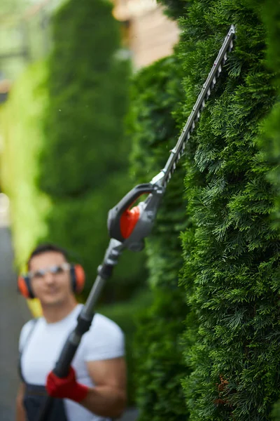 Caucasian man trimming hedge with petrol cutter. — Foto de Stock