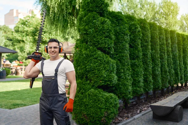Muscular gardener holding electric hedge trimmer outdoors — kuvapankkivalokuva