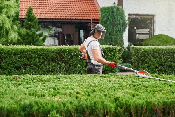 Strong man in uniform using electric hedge trimmer for work — Foto de Stock