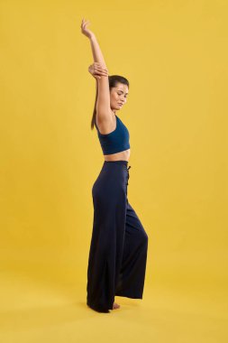 Sıska kız ayakta, elini kaldırıyor, aşağıya bakıyor.,