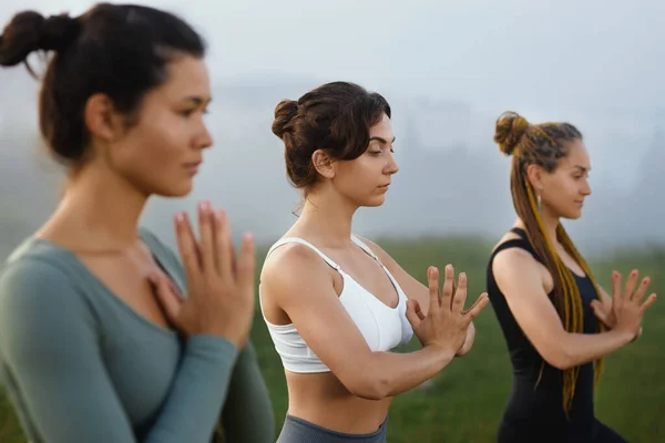 Woman in white top meditating among blurring females in morning foggy nature. — Foto Stock