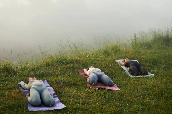 Group of women lying down practising supta vajrasana pose on morning nature. — Stock Photo, Image