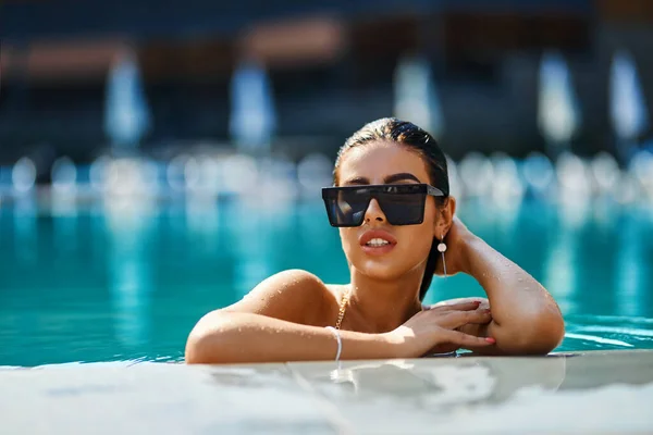 Λαμπερή γυναίκα με κομψά γυαλιά ηλίου που απολαμβάνει το κολύμπι σε τυρκουάζ νερά. — Φωτογραφία Αρχείου