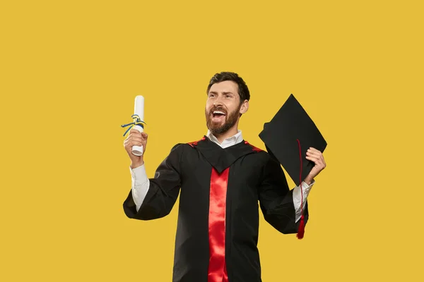 Male student graduating, holding diploma and mortarboard, showing hurray. — Photo