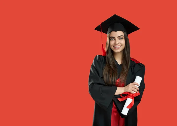 Girl in graduate gown and mortarboard standing, holding diploma. — ストック写真