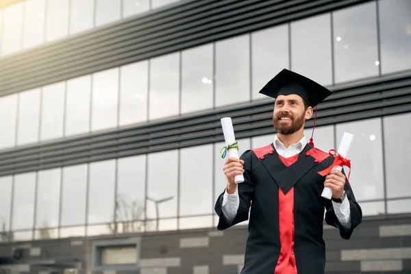 Student v miniaturních a absolventských šatech se dvěma diplomy. — Stock fotografie
