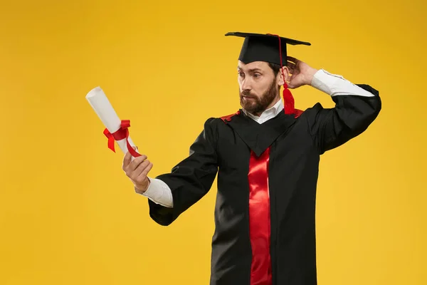 Student stojící, dívající se na diplom, zmatený, překvapení. — Stock fotografie