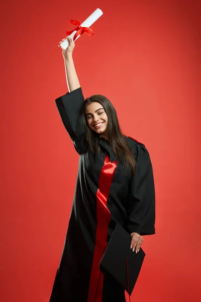 Дівчина в сукні стоїть, піднімає руку, тримає диплом , — стокове фото