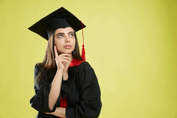 Girl in mortarboard and graduate gown standing, thinking. — Foto Stock