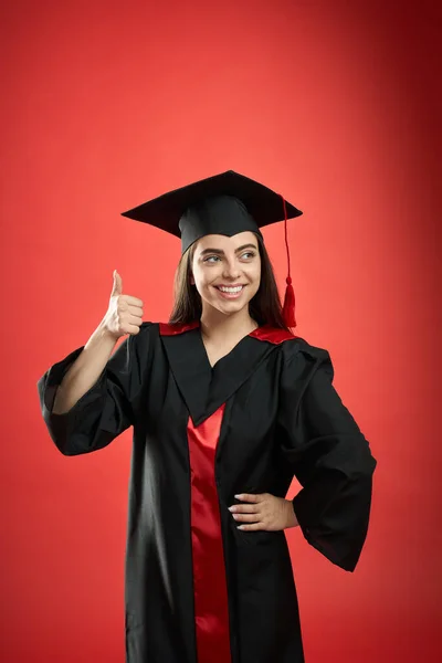 Girl in graduate gown and mortarboard standing, showing super. — Stockfoto