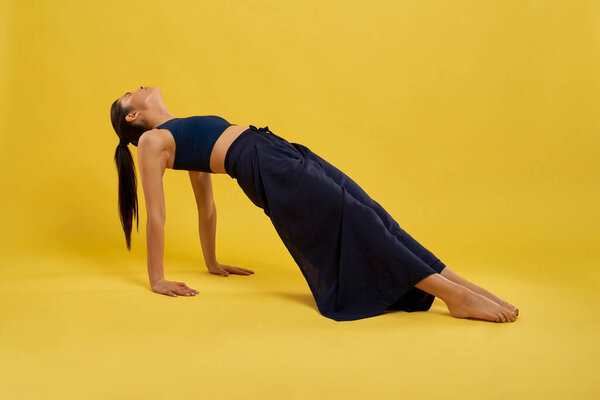 Fit girl stretching body at upward plank pose of yoga indoors.