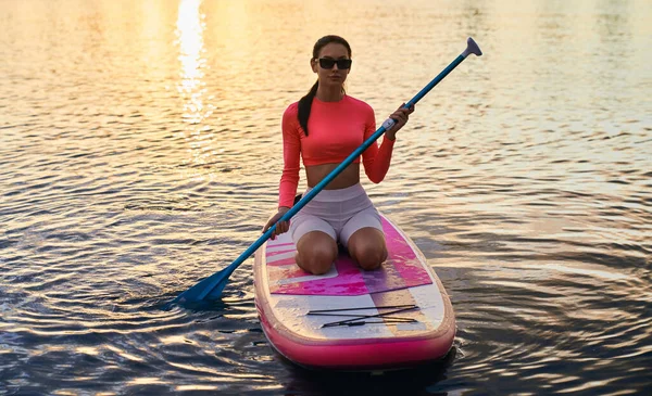 Young woman sitting on sup board on city lake — Stockfoto