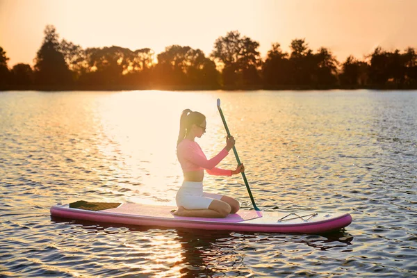 Woman in sportswear rowing with paddle on sup board
