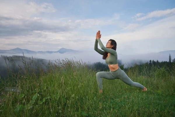 Giovane donna che pratica yoga tra le montagne verdi — Foto Stock