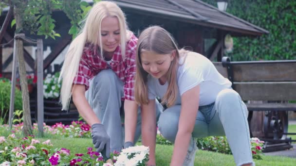 Boldog szőke anya tanítja tinédzser lányát virágot ültetni a kertbe. — Stock videók