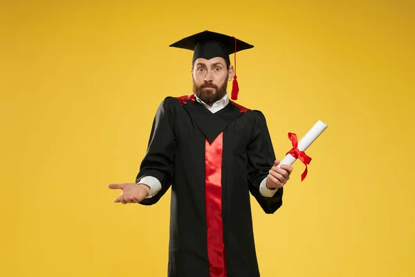 Masculino com barba em pé, segurando diploma, surpreso, misturado. — Fotografia de Stock
