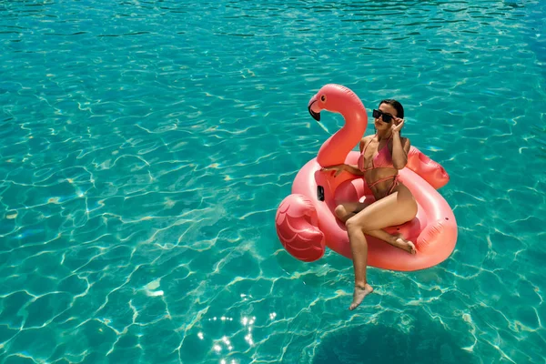 Brünettes Mädchen schwimmt im Pool und sitzt auf rosa Flamingo. — Stockfoto
