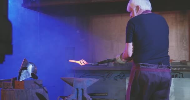 Starý muž s šedivými vlasy a vousy pracuje v kovárně. — Stock video