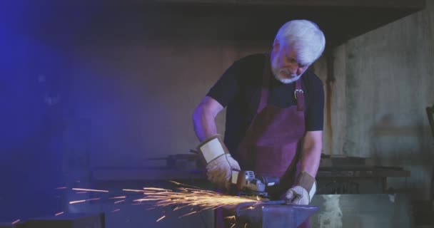Starý muž s šedými vlasy pracuje jako kovář. — Stock video