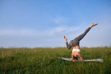 Güçlü bir kadın doğada amuda kalkmaya çalışıyor. 