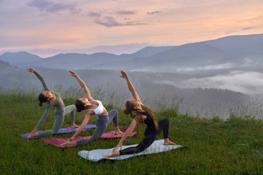 Dağların arasında yoga egzersizleri yapan sportif kadınlar.
