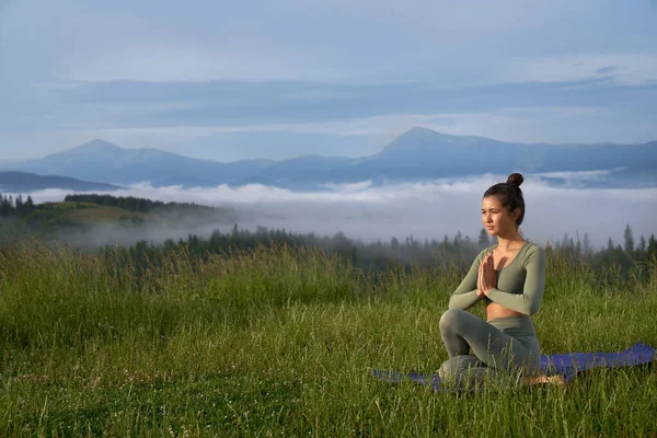 Donna seduta su tappetino yoga e meditando tra le montagne — Foto Stock