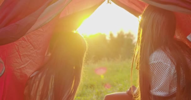 Baksidan av flickor sitter tillsammans, ser ut av röd tio, njuter av solnedgången, landskap och vacker natur, prata. Barn som campar i bergen. Begreppet naturens skönhet — Stockvideo