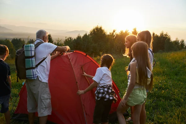 Alter Mann baut mit Kindern rotes Zelt auf. — Stockfoto