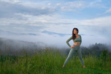 Güzel dişilerin arka planda dağlarla esneme hareketleri vardır..