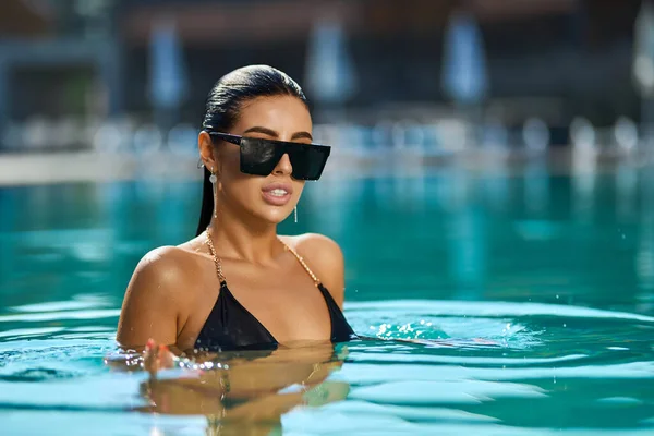 Σέξι μελαχρινή γυναίκα που φοράει μαύρο μπικίνι χαλαρώνοντας στην πισίνα έξω. — Φωτογραφία Αρχείου