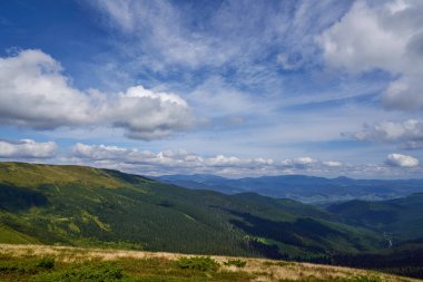 Güneşli bir günde yeşil orman tepeleri ve dağ tepeleri olan manzaralı bir yer..