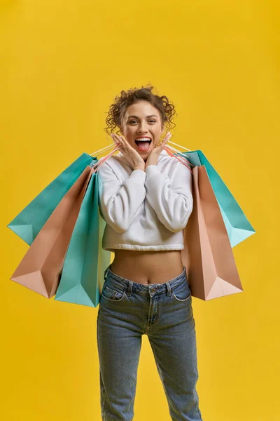 Female shopaholic showing positive emotions, enjoying purchases inside. Portrait view of beautiful lady in good mood after best shopping, isolated on yellow studio background. Concept of lifestyle.
