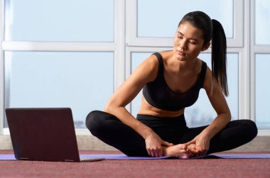 Çıplak ayaklı genç bir kadının evde yoga dersi alması ön planda. Kelebek 2 yoga pozu veren güzel bir kız interaktif dersler sırasında dizüstü bilgisayara bakıyor. Yoga pratiği kavramı.