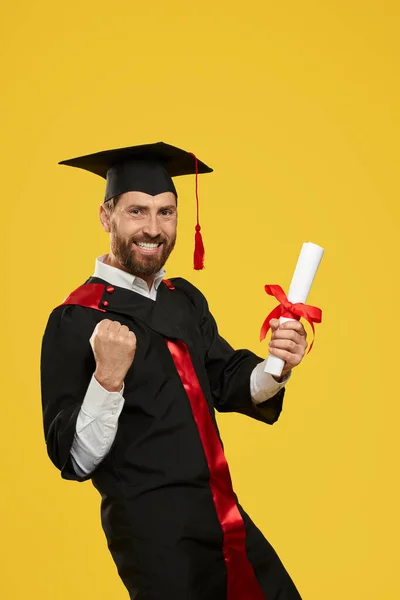 高校を卒業する幸せな学生の側面図 ひげを生やした少年は 立って カメラを見て 笑みを浮かべて 卒業証書を保持し 急いで示しています 黄色の背景に隔離された — ストック写真