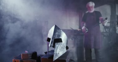 Eski demircinin şövalye zırhı dövdüğü ön manzara. Demir miğfer, maske, gri saçlı ve sakallı bir adam, bakıyor. Sanatçılık ve kalpazanlık kavramı.