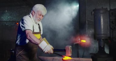 Metal işçiliğinde çalışan yetenekli bir demircinin ön görüntüsü. Güçlü erkek sopası kancayı tutuyor, dövüyor, çekiç gibi yükseliyor, dövüyor. El işçiliği ve işçilik kavramı.