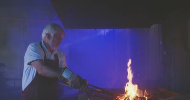 냄새로 일하는 남자의 측면시야 대장장이는 앞치마를 장갑을 가마에서 작업을 불꽃을 — 비디오