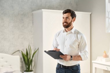 Sakallı esmer erkek mobilya tasarlıyor, iç mekan. Yakışıklı satıcı, tasarımcı, mimar ayakta duran, klasörü tutan, yazan, yukarı bakan. Tasarım kavramı.