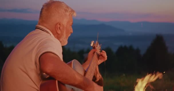 一边看老人弹吉他 一边用大胡子唱歌 头发灰白的男人坐在红色帐篷附近 孩子们在听歌曲 旅行与自然和谐的概念 — 图库视频影像