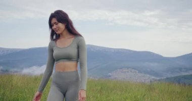 Aktif kıyafetli genç bir kadın yoga antrenmanından sonra sahada yürüyor. Siyah saçlı kadın meditasyondan sonra huzurlu zihnin tadını çıkarıyor. Açık hava eğitimi. 