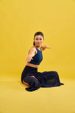 Stüdyoda yoga pozisyonunda otururken sağ kolunu uzatan ciddi bir kız. Uzaktan bakan bir kadının portre görüntüsü, yoga çalışması, turuncu stüdyo arka planında izole edilmiş. Egzersiz kavramı.