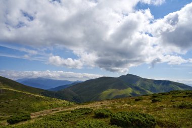 Yazın yeşil orman tepeleri ve dağ zirveleri olan güzel bir dağ manzarası. Arka planda bulutlu gökyüzü ile nefes kesen dağ sırasının en üst görüntüsü. Dağ manzarası kavramı.